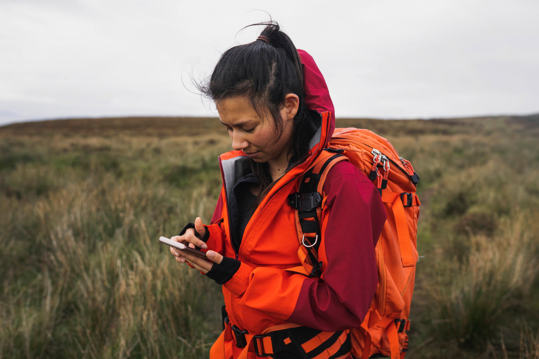 Eine Frau in Funktionsbekleidung schaut auf einer Wiese auf ihr Smartphone